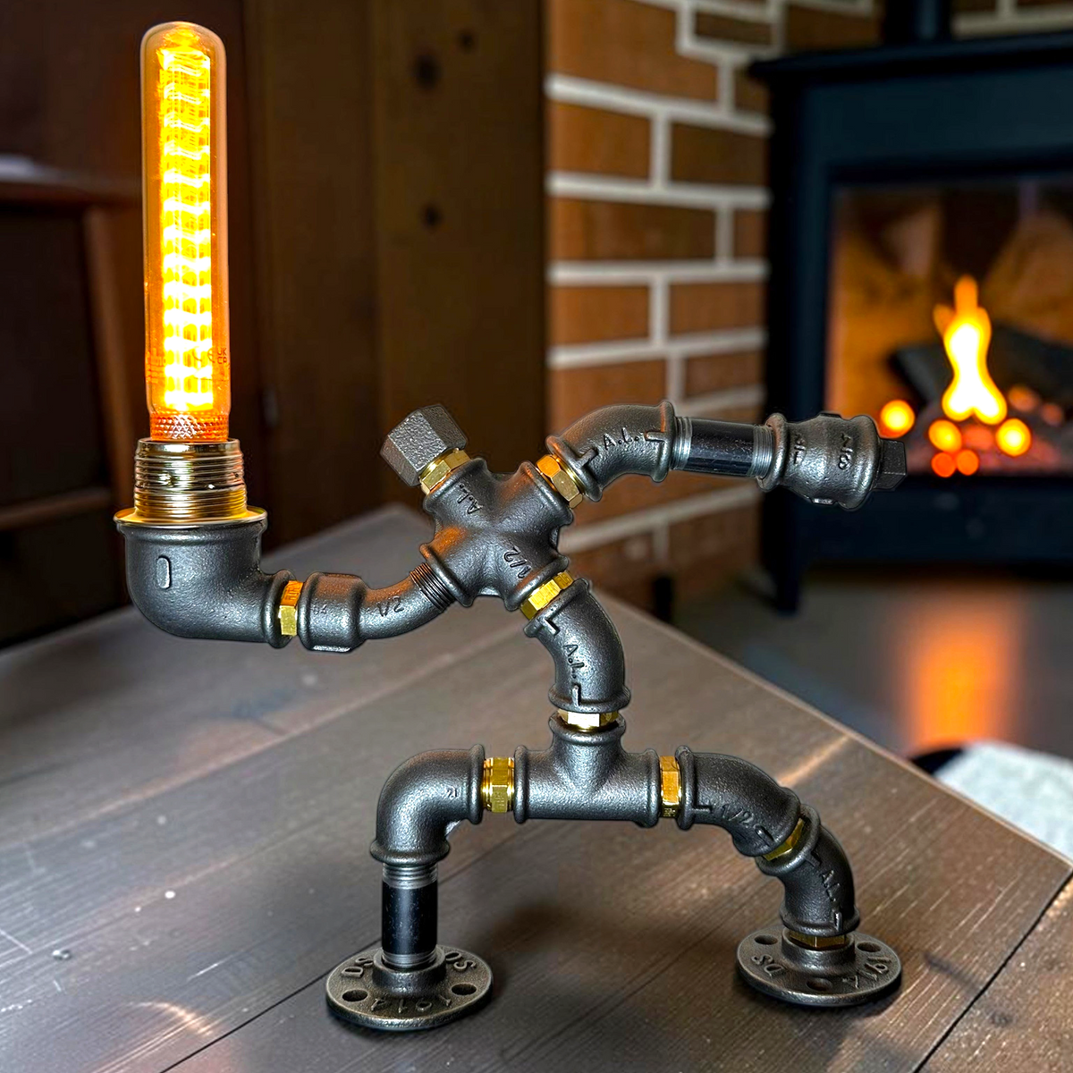 IronPunky Hampelmann Tischlampe aus schwarzem Industrierohr mit Edison-Glühbirne vor einem Kamin