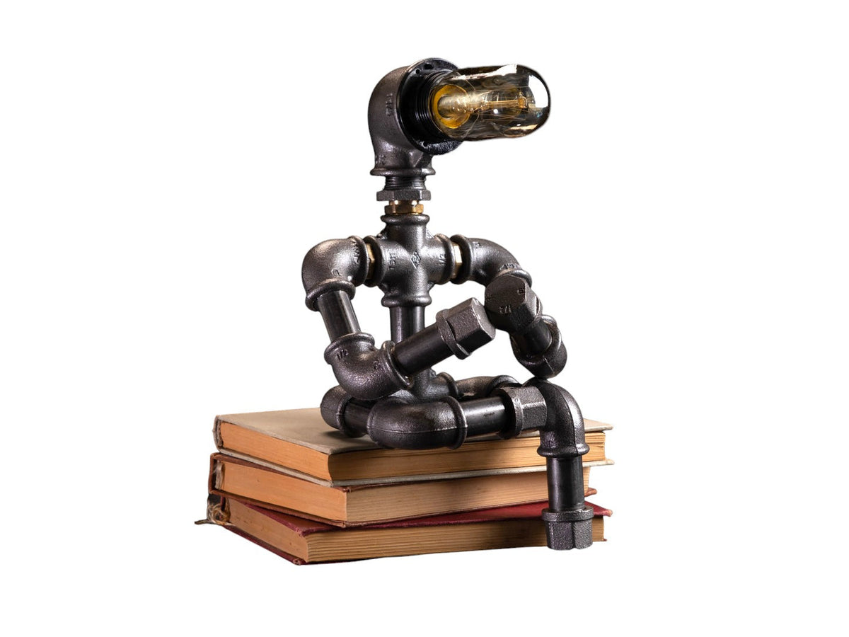 IronPunky Kapitelträumer Tischlampe aus schwarzem Temperguss in Form einer sitzenden Figur auf einem Bücherstapel