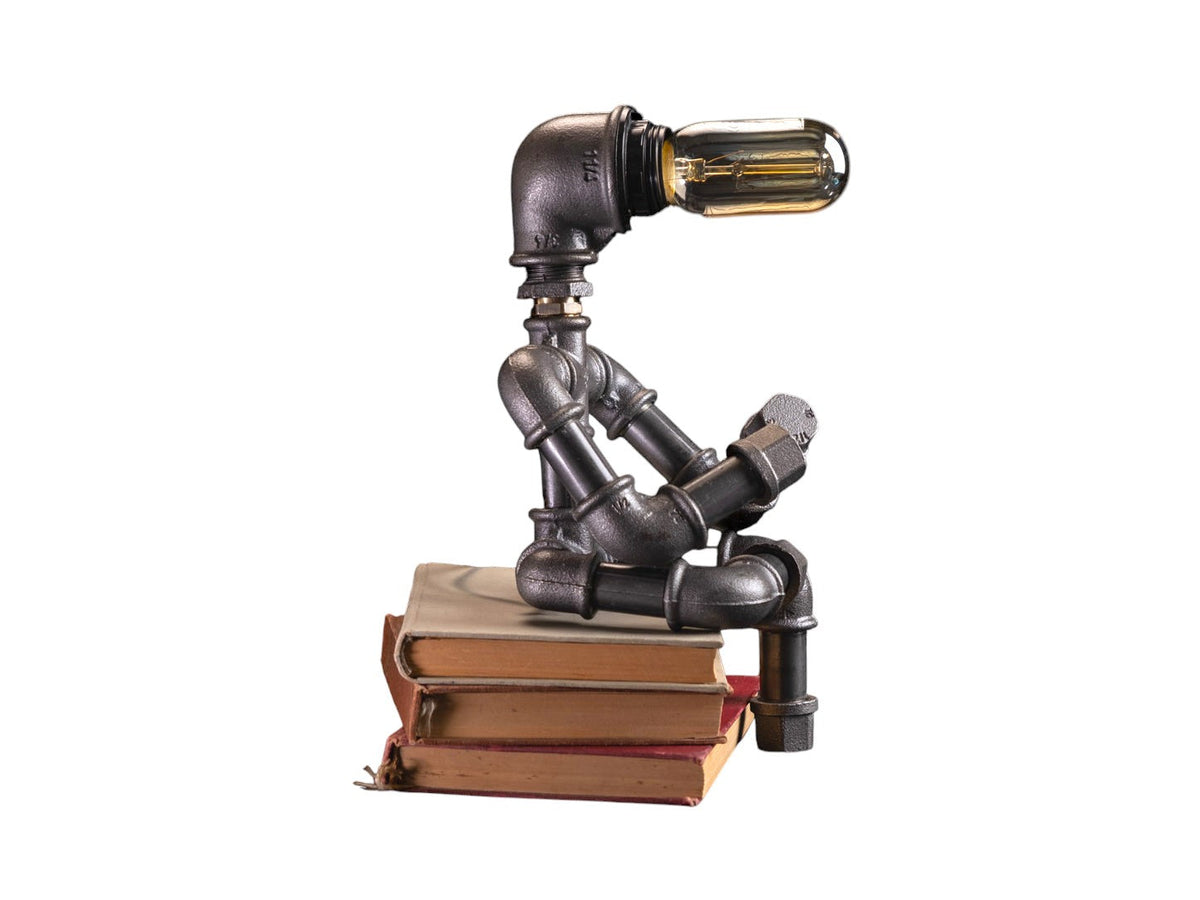 IronPunky Kapitelträumer Tischlampe aus schwarzem Temperguss in Form einer lesenden Figur auf alten Büchern