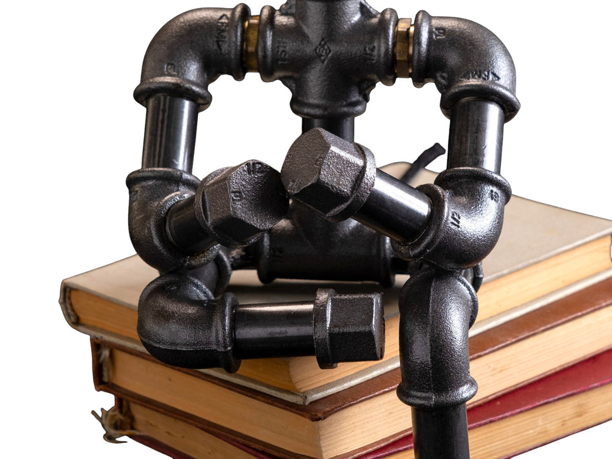 IronPunky Kapitelträumer Tischlampe aus schwarzem Temperguss in Form einer sitzenden Figur auf alten Büchern