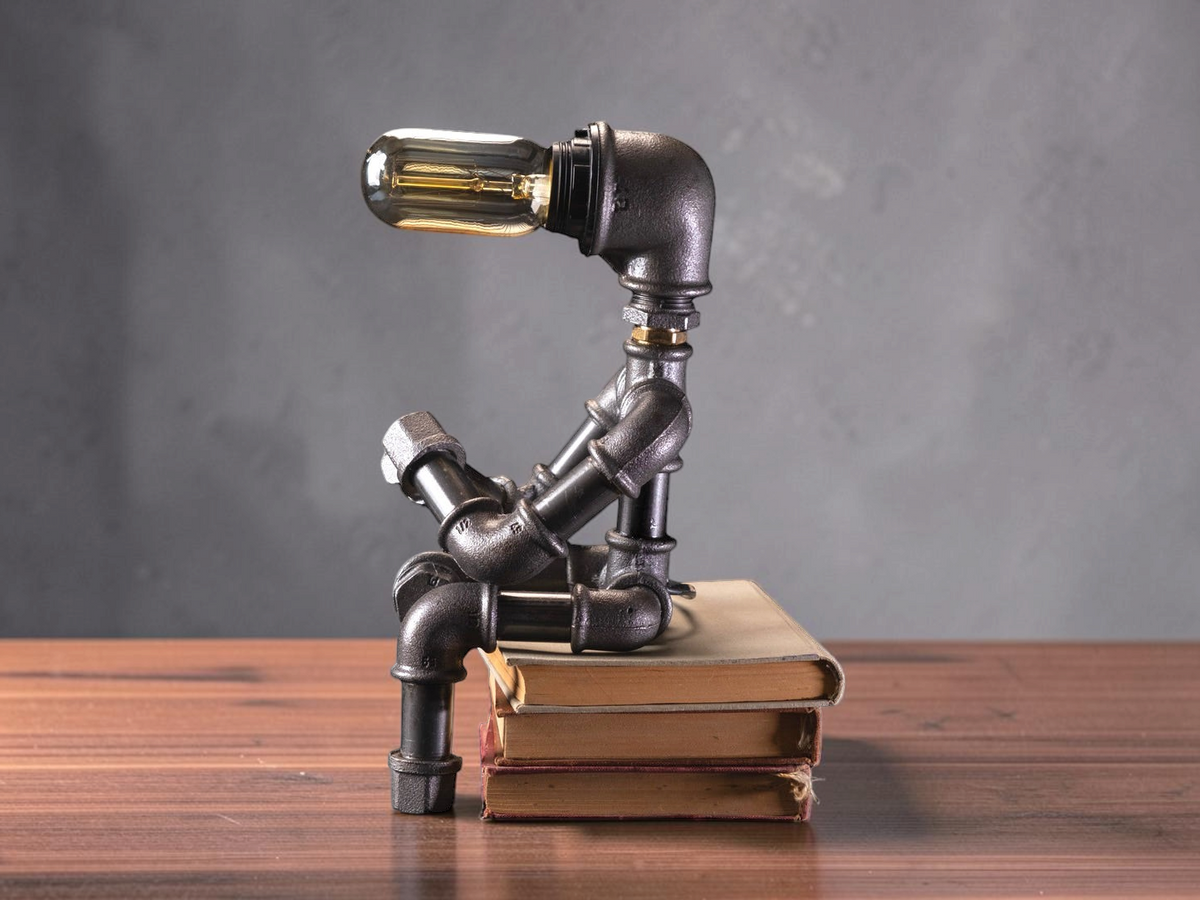 IronPunky Kapitelträumer Tischlampe aus dunklem Temperguss in Form einer lesenden Figur auf einem Bücherstapel